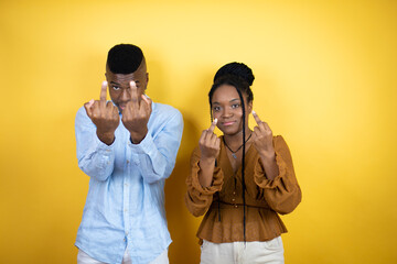 Young african american couple standing over yellow background showing middle finger doing fuck you...