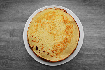 Pancakes on a white plate top view on a table with a wooden texture
