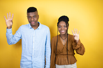 Young african american couple standing over yellow background showing and pointing up with fingers number four while smiling confident and happy