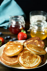 Blini served with strawberry jam, honey, sour cream and fresh berries. Dark wooden table, high resolution