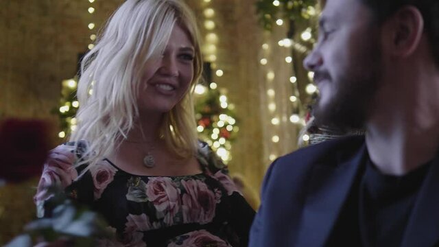 attractive blonde runs rose on bearded man chest and hugs against decorated Christmas tree with illumination slow motion