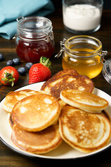 Blini served with strawberry jam, honey, sour cream and fresh berries. Dark wooden table, high resolution