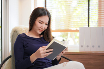 Close up of young asian woman sitting to relaxing on comfortable armchair and reading book while...