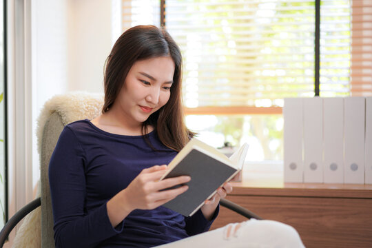 Close up of young asian woman sitting to relaxing on comfortable armchair and reading book while rest
