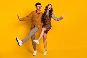 Full length photo of funny happy man and woman couple look empty space dance raise leg isolated on yellow color background