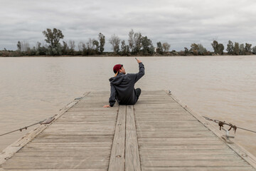 Young man taking a selfie sitting in a pier