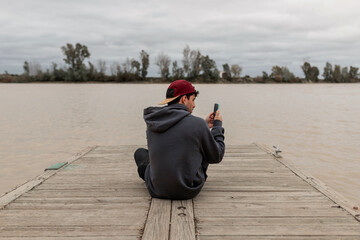 Young man using a smartphone sitting in a pier