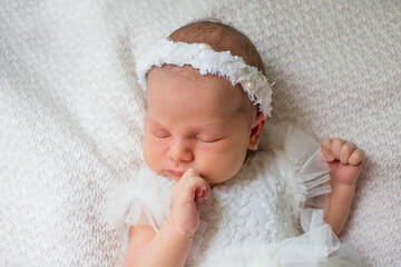 Newborn baby girl sleeping on a white blanket in a dress and wreath.