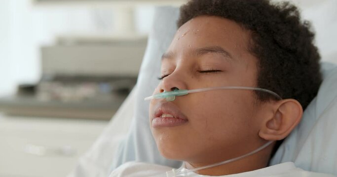 Close up of afro-american preteen boy with nasal cannula having fever and sleeping in hospital bed