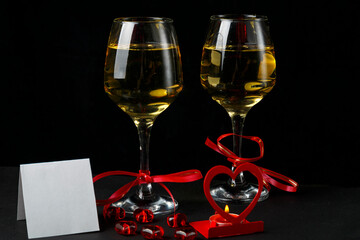 Glasses with champagne tied with a red ribbon on a black background greeting card and a candlestick in the shape of a heart