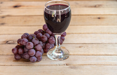 Bunch of pink grape and glass of natural juice on wooden background