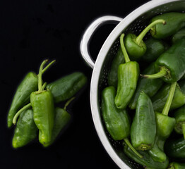A pile of raw Padron peppers typical of Spain. Peppers in a colander on a black background. Flat lay. Top view.