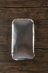 Closed aluminum foil plate of sushi rolls placed on wooden surface