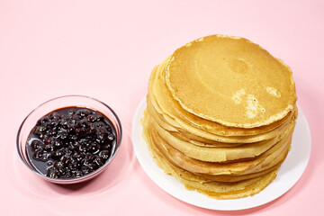 a stack of Russian pancakes and a bowl of cherry jam on a pink background, pancakes for Shrovetide before Lent