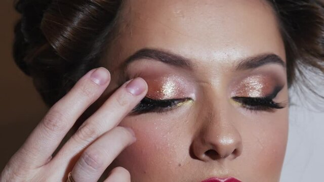 The makeup artist applies bronze shadows on the female eye with a brush. Close-up of smokey eyes of a young woman