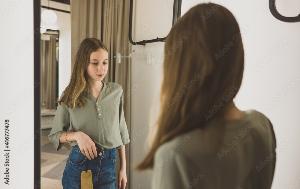 Wall mural tween girl standing in fitting room in clothing store.