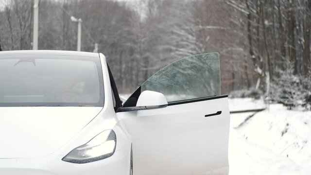 Gybrid car, Tesla. Fashionable woman getting into the car. Winter season.