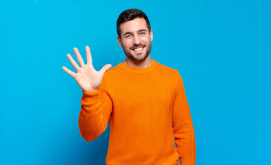 handsome adult blond man smiling and looking friendly, showing number five or fifth with hand...