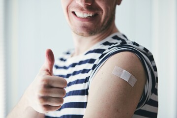 Happy young man showing thumb up and his arm after vaccination. Themes prevention, vaccine and health care during pandemic covid-19. - obrazy, fototapety, plakaty