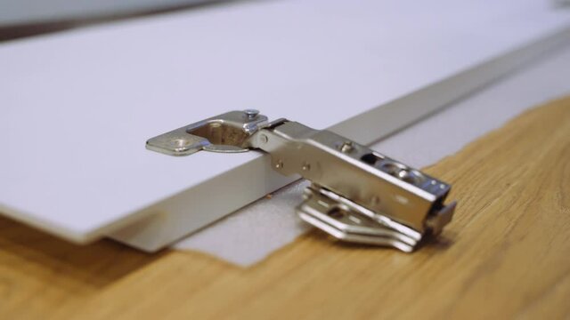 Carpenter man screws hinge to furniture door using electric screwdriver.