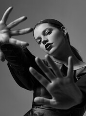 Beautiful young girl with bright lipstick in a black leather dress posing in the studio. Emphasis on the hands.