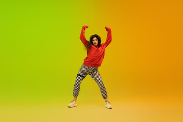Fototapeta na wymiar Dynamic. Stylish sportive girl dancing hip-hop in stylish clothes on colorful background at dance hall in neon light. Youth culture, movement, style and fashion, action. Fashionable bright portrait.