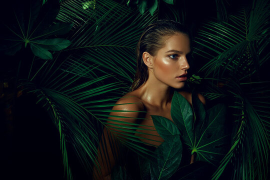 A beautiful tanned girl with natural make-up and wet hair stands in the jungle among exotic plants