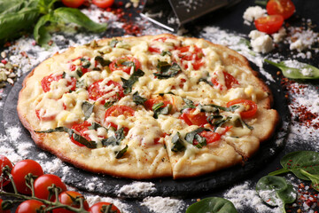 Italian cuisine. Pizza with cheese, tomatoes, basil and spices on a black board with flour, oil and ingredients. Background image, copy space, horizontal