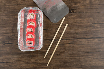Aluminum foil plate of sushi rolls with red caviar on wooden surface
