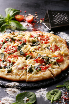 Italian cuisine. Pizza with cheese, tomatoes, basil and spices on a black board with flour, oil and ingredients. Background image, copy space, vertical