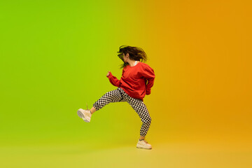 Fototapeta na wymiar Action. Stylish sportive girl dancing hip-hop in stylish clothes on colorful background at dance hall in neon light. Youth culture, movement, style and fashion, action. Fashionable bright portrait.