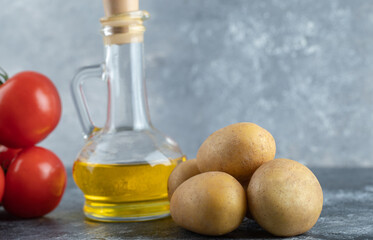 Bottle of olive oil, potatoes and tomatoes on marble background