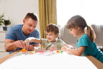 Obraz premium Dad with two kids playing animal figures together at home. Family having fun playing at home. stay home concept