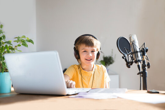 Smiling schoolboy using headphones in front of microphone talking and recording podcast in home creating content for online blog.  blogging concept.

