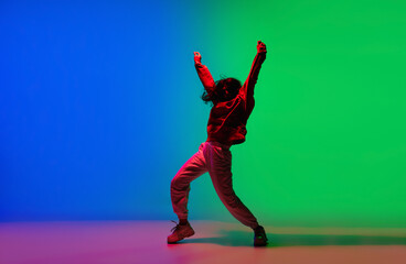 Modern. Stylish sportive girl dancing hip-hop in stylish clothes on colorful background at dance hall in neon light. Youth culture, movement, style and fashion, action. Fashionable bright portrait.