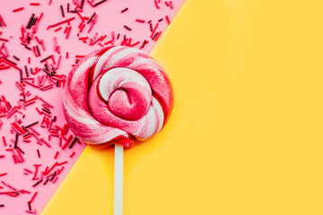 Colorful lollipop with sugar topping isolated over pink and yellow paper background. Flat lay. Copy space. Minimal concept
