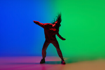 Modern. Stylish sportive girl dancing hip-hop in stylish clothes on colorful background at dance hall in neon light. Youth culture, movement, style and fashion, action. Fashionable bright portrait.