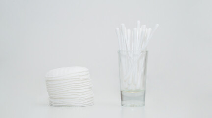 Close-up of stack of cotton pads and cotton swabs in a glass cup. White background.