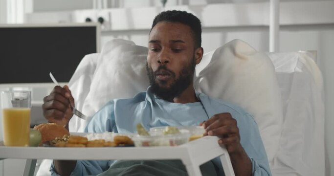 African male patient in hospital bed eating meal from tray