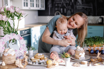 family with child celebrates easter. Happy mom and baby at the festive table. Easter eggs and cake. Set table with decor for a traditional dinner. Spring Christian holiday. Happiness laughter mood