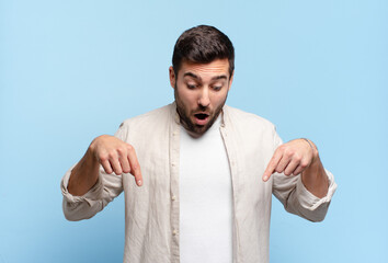 handsome adult blond man feeling shocked, open-mouthed and amazed, looking and pointing downwards...