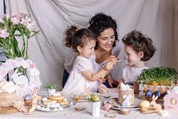 Happy family is preparing for Easter. Mother and children paint eggs together for fun. joy life moments lifestyle. Festive dinner on a decorated table. Mix race kids. Christian traditions of spring