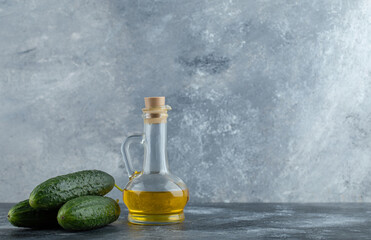 Stack of fresh cucumber and bottle of oil over grey background