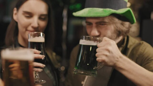 Slow-motion medium close-up of happy company of friends toasting beer glasses celebrating St Patricks Day in local Irish pub