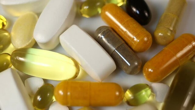 White, yellow, brown, transparent, black, oval and oblong tablets, pills and capsules, water and fat-soluble. Close-up, real time, raked in a pile