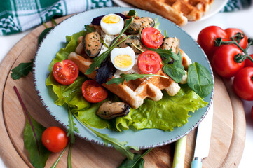 Belgian waffles with mussels, tomatoes, eggs and green salad, arugula, spinach on blue plate