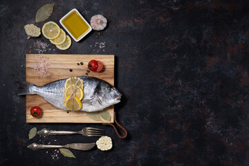 fresh dorado fish on a wooden board with cutlery. on a dark background. cooking with cherry tomatoes, olive oil, lemon, chili, garlic, salt, pepper. dish of the Mediterranean diet