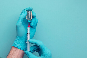 Doctor or nurse wearing blue surgical gloves holding a syringe and vaccine dose