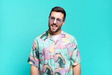 young handsome adult man looking happy and friendly, smiling and winking an eye at you with a...
