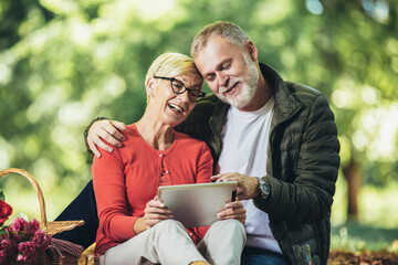 Happy senior couple having a picnic in park using digital tablet